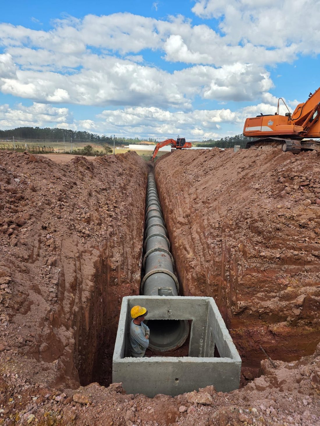Rede de drenagem em vala profunda, com operário em pé dentro da caixa de concreto