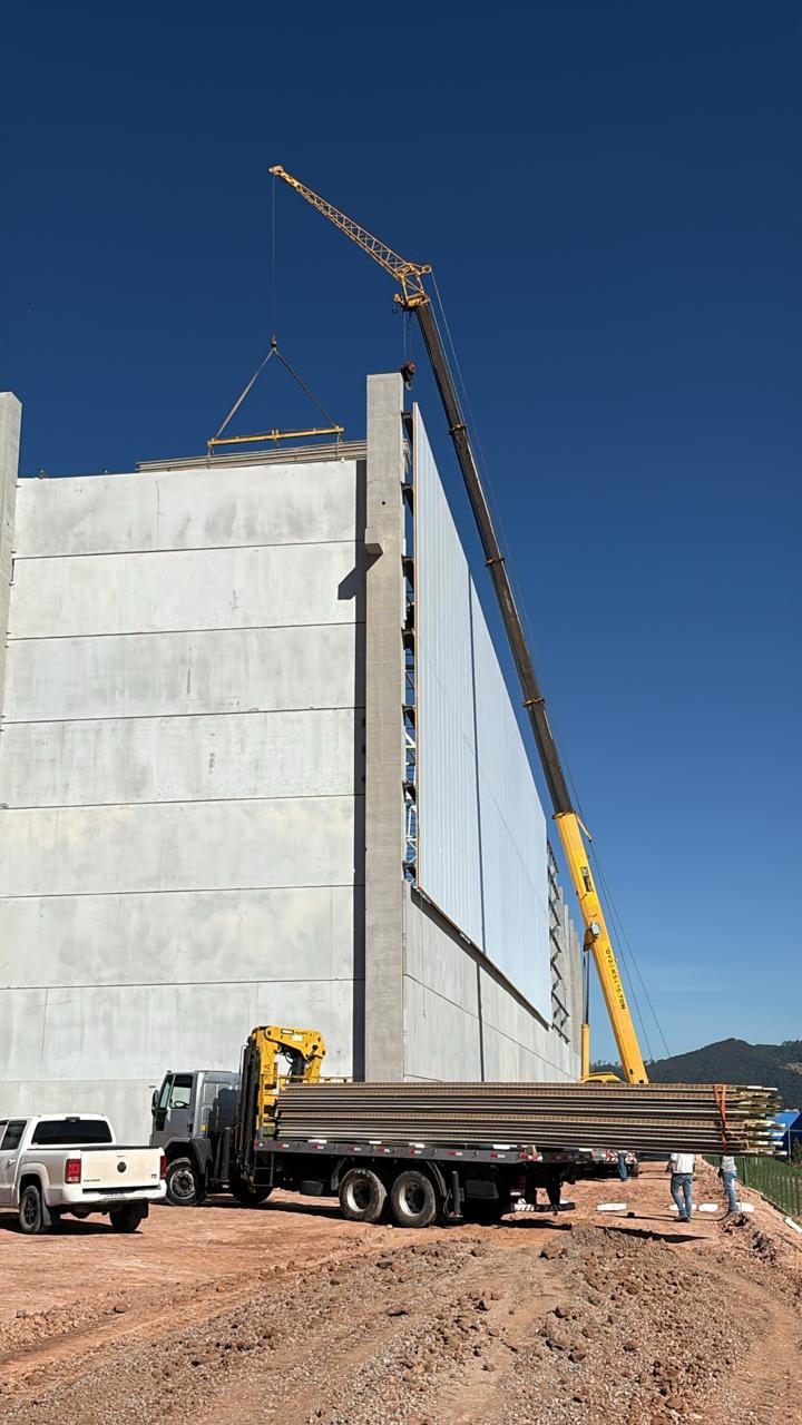 Caminhão munck içando painel no alto da parede, com o fardo de painéis na carroceria
